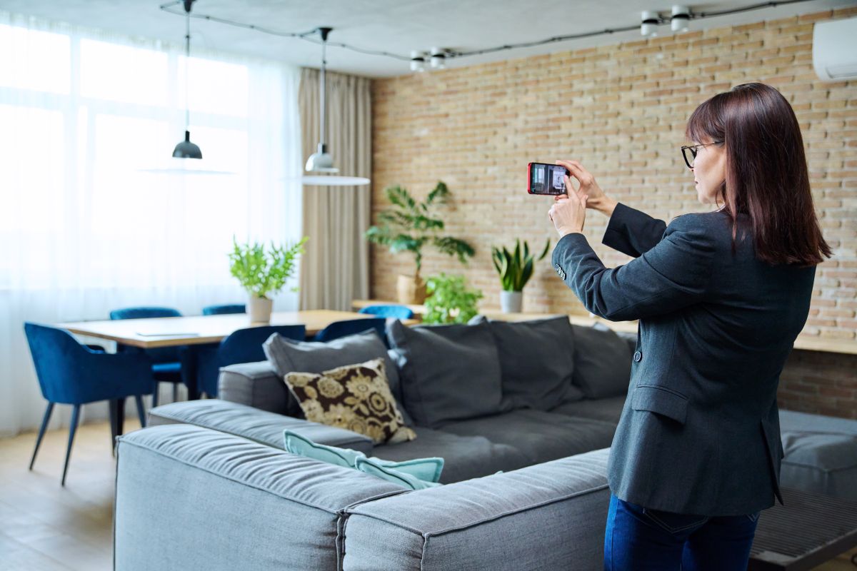 femeie face poze cu telefonul intr-un apartament pentru a-l lista la vanzare