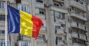 drapelul romaniei si un bloc vechi de locuinte in fundal