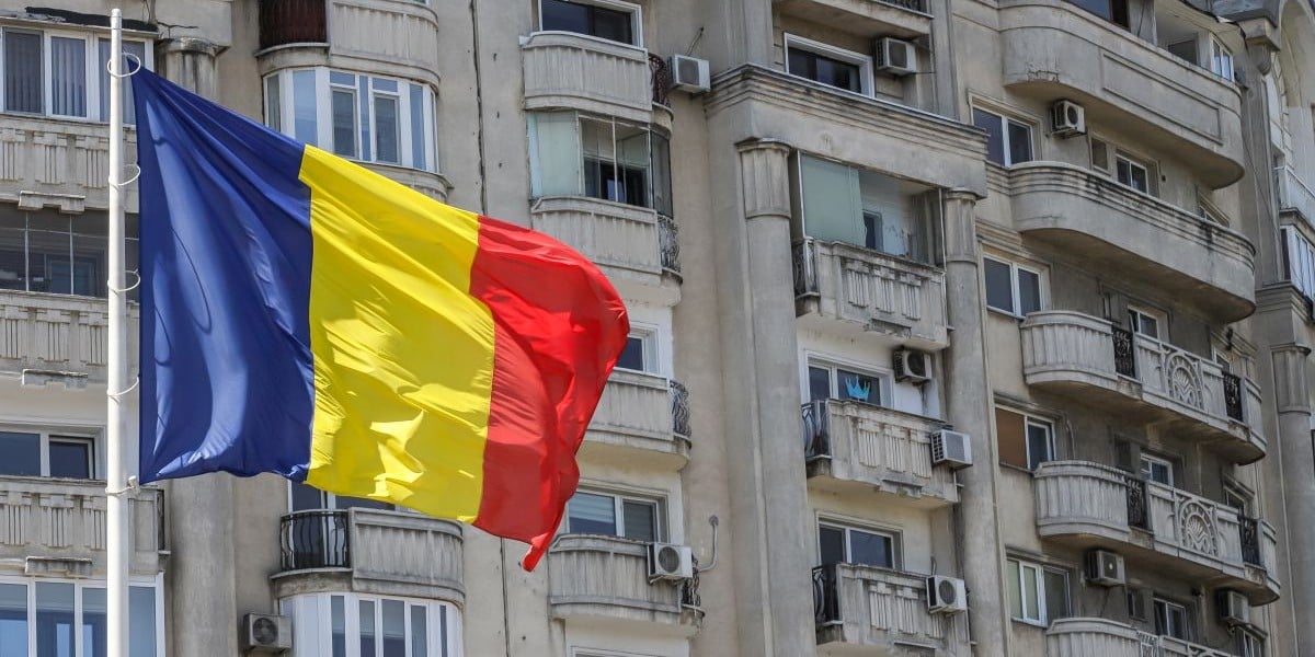 drapelul romaniei si un bloc vechi de locuinte in fundal